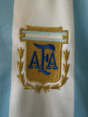 Soccer jersey crest badge on chest, blue and gold shield with stylized letters