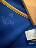 Blue football shirt fabric closeup with gold trim and size care label