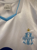 White Olympique Marseille home shirt with blue V-neck trim, adidas logo, and crest.